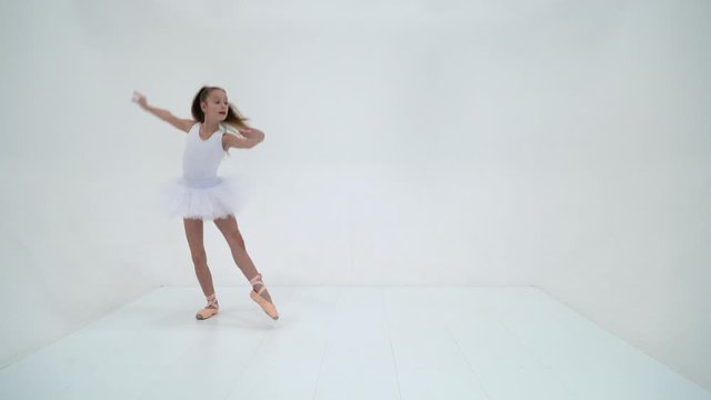 Charming little girl in a bundle and pointe shoes is dancing in the studio. Isolated over white background.