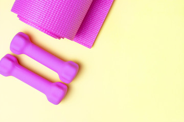Pink sports mat and dumbbells on yellow background, copy space