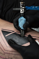 Professional tattoo artist makes tattoo on man leg. Process. Introduces black ink into skin using needle from tattoo machine. Close up of tattoo machine. Tattooing. Master creating picture on leg.