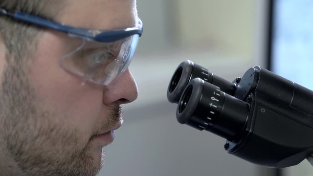 closeup of male doctor in safety goggles examining sample with microscope Spbas. Coronavirus epidemic, virus vaccine concept. laboratory professional scientist is working