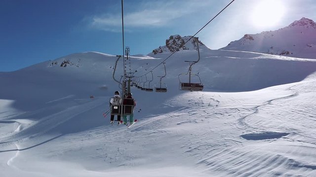 Two skiers riding a chair lift to the summit of Silvretta Montafon Ski Arena Austria, slow motion