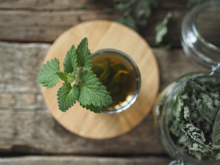 Medicinal herbal tea using dried Melissa. Dried leaves of Melissa or mint with a fresh twig and decoction in a glass on an wooden table.