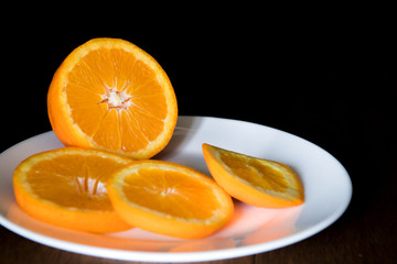 Oranges and Orange Slices on white plate. Healthy Citrus Fruit. Dark Scene.
