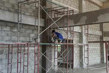 Construction worker sit on scaffolding and plastering building wall and beam at the construction site.