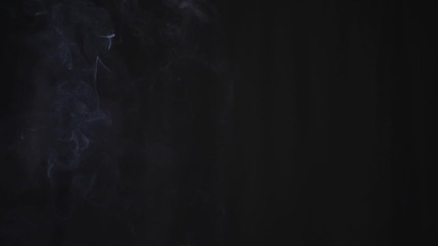 white cigarette smoke rises slowly against black background