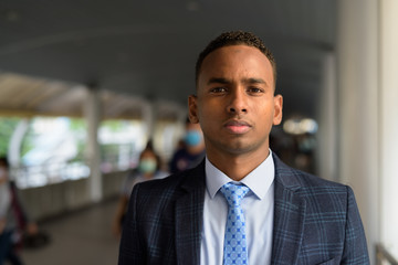 Fototapeta premium Face of young handsome African businessman wearing suit at footbridge in the city