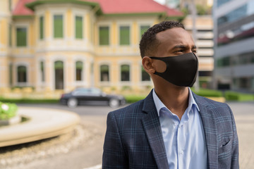 Fototapeta premium Face of young African businessman with mask for protection from corona virus outbreak thinking outdoors