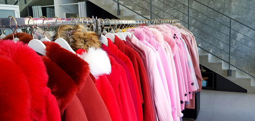 Sweet pink and red winter coats hanging on stainless steel hanger for rent with copy space. Colorful sweater for sale at shopping store or market. Winter season cloth fashion design background.