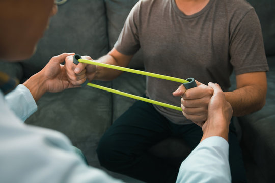 Patient doing stretching exercise with a flexible exercise band and a physical therapist hand to help in clinic room.