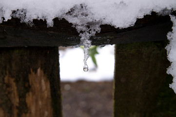 Melting icicle and fresh snow on a wooden frame