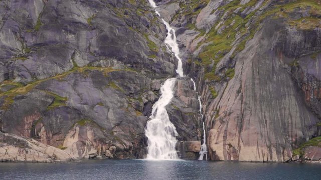 Waterfall through snow covered mountains in prince Christian sound in Greenland filmed from a cruise ship in slow motion