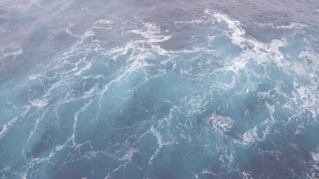 Ice blue water rushing past the bow of a sailing cruise ship with white foam splashing past, filmed looking directly down at 120fps slow motion