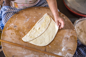Woman in a black chef's apron roll out the dough for preparing Turkish pancake. 
Woman rolls out...