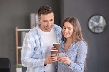 Young colleagues with mobile phone drinking coffee in office