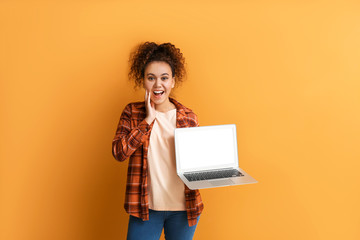 Surprised young African-American woman with laptop on color background