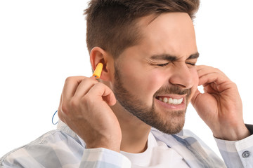 Young man with ear plugs suffering from loud noise on white background