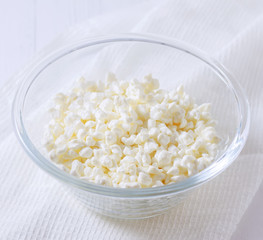 Cottage cheese. Fresh natural cottage cheese in a glass cup stands on a light table.