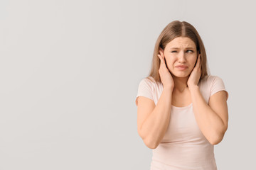 Young woman suffering from loud noise on light background