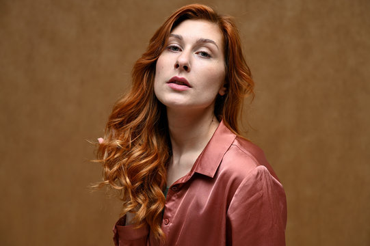 A pretty model is wearing a red shirt. Portrait of actress caucasian woman with red hair showing serious emotions. Photo taken in the studio on a beige background.