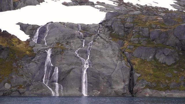 Waterfall through snow covered mountains in prince Christian sound in Greenland filmed from a cruise ship in slow motion 120fps