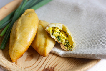 pies with green onions and an egg lie on a wooden plate. rustic breakfast. fresh bakery. broken pie stuffed with yellow-green