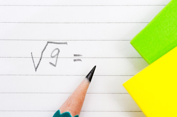 A green simple pencil lies on the surface of the notebook with the inscription, the formula square root of 9 and yellow and green stickers.