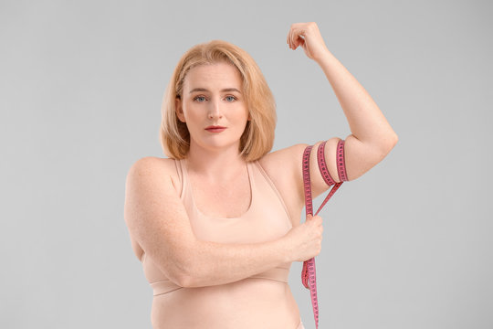Overweight woman with measuring tape on grey background. Weight loss concept