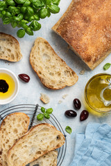 Ciabatta with olive oil, basil and black olives on a blue background. Traditional italian bread. Sliced ciabatta. Top view