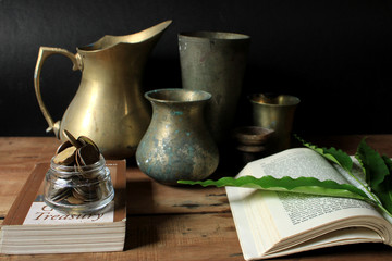 Old vintage utensils with book and Indian rupee coins. Old brass metal utensils on wooden table...