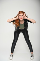 Naklejka premium Model in various poses on a white background in the studio. Full-length vertical portrait of a pretty caucasian woman with excellent make-up with long red hair in a black jacket and trousers.