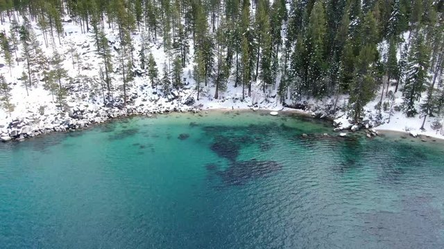 High-res 4K drone footage reveals clear waters of Lake Tahoe in a secret bay in California. A small cove lies on the east shore of the Sierra Nevadas in the mountains lined with trees and snow.
