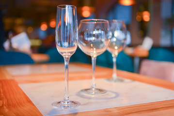 Transparent empty champagne and wine glasses on the rustic wooden table over blurred restaurant background.