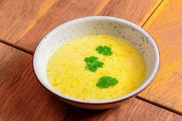 Chicken soup with vegetables served in a white bowl over rustic wooden background.