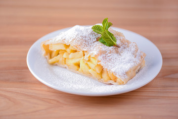 Delicious slice of freshly baked apple pie on a white plate over light rustic wooden table. Sweet dessert.