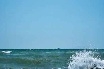 Image of the sea shore. In the background is a warship.