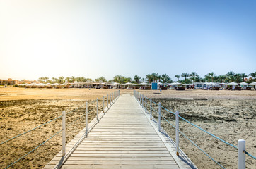 Fototapeta premium Wooden pier leading to the shore on a sunny day/beautiful wooden pier at the sea leading to the shore with blue sky