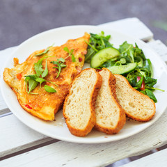 Smażone jajka, omlet, potrawa na śniadanie, biały talerz, dodatki sałatka i warzywa oraz pieczywo.