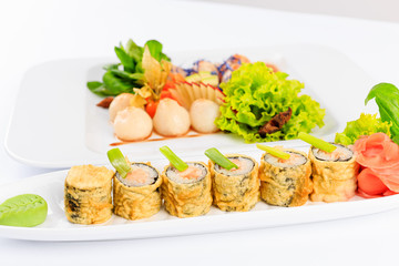 Sushi, danie kuchni japońskiej, podane na białym talerzu, dodatki warzywa i sałaty.
