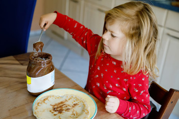 Cute little toddler girl eating homemade fresh crepes or pancakes with chocolate cream for...