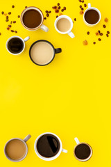 Different cups of coffee on yellow table top-down space for text