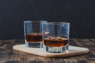 Two Glasses of whiskey with ice cubes on a wooden table/Two Glasses of whiskey with ice cubes on a wooden table. Black background with copyspace.