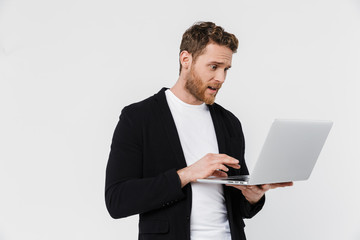 Image of handsome surprised man in jacket holding and using laptop