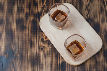 Two Glasses of whiskey with ice cubes on a wooden table/Two Glasses of cognac with ice cubes on a wooden table. Top view, copyspace