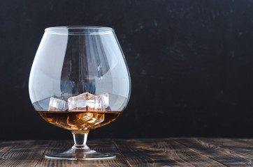 Glass of cognac with ice cubes on a wooden bar/Glass of cognac with ice cubes on a wooden bar. Black background with copyspace.