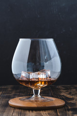 Glass of cognac with ice cubes on a wooden surface/Glass of cognac with ice cubes on a wooden surface. Selective focus