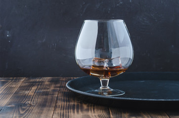 Glass of brandy with ice cubes/Glass of brandy with ice cubes on a black tray. Black background with copyspace.