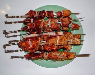 juicy pork skewers on a green dish on a white background