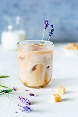 Glass of coffee with ice, milk and lavender flowers on a light background. Cold summer drink.