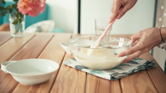 Cooking recipe footage. Close Up shot of a woman's hands mixing cream or dough with a silicone spatula in a glass bowl. Cooking at home.