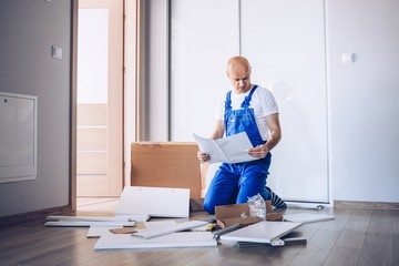 Nervous man assembling cabinet and reading manual